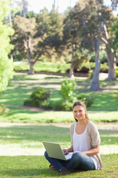 Leende kvinna som sitter på gräsmattan med sin laptop — Stockfoto