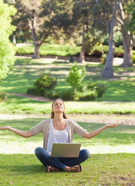 Kvinna sitter på gräsmattan i en yoga position med en bärbar dator — Stockfoto