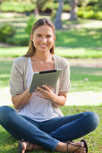 Улыбающаяся женщина сидит на лужайке со своим планшетным компьютером — стоковое фото