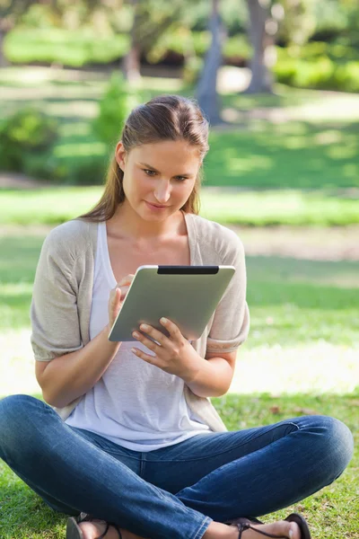 Frau sitzt im Gras, während sie ihren Tablet-Computer benutzt — Stockfoto