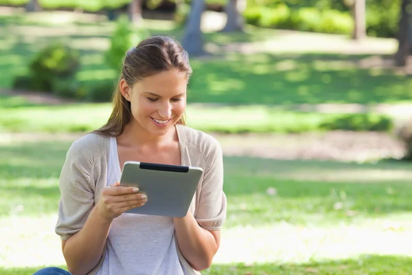 Улыбающаяся женщина с планшетным компьютером, сидящая на газоне — стоковое фото