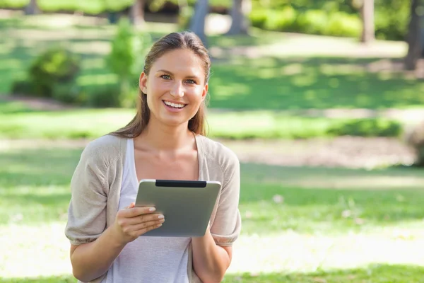 Улыбающаяся женщина в парке с планшетным компьютером — стоковое фото