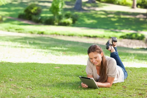 Улыбающаяся женщина лежит на газоне с планшетным компьютером — стоковое фото