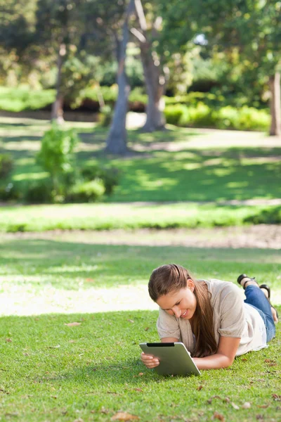 Женщина лежит на газоне с помощью планшетного компьютера — стоковое фото