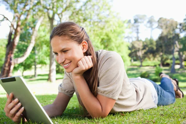 Усміхнена жінка лежить на газоні зі своїм планшетним комп'ютером — стокове фото