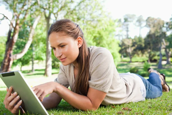 Frau mit Tablet-Computer auf dem Rasen liegend — Stockfoto