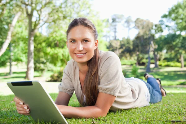 Улыбающаяся женщина с планшетным компьютером, лежащим на лужайке — стоковое фото