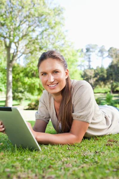 Улыбающаяся женщина лежит на траве со своим планшетным компьютером — стоковое фото