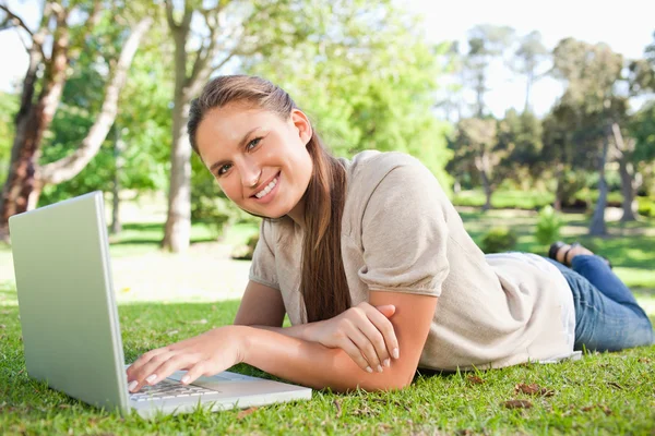 Улыбающаяся женщина лежит на лужайке со своим ноутбуком — стоковое фото