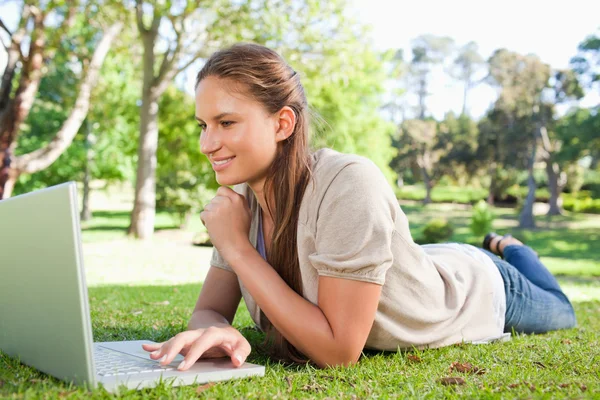 Lächelnde Frau mit ihrem Notizbuch auf dem Rasen liegend — Stockfoto