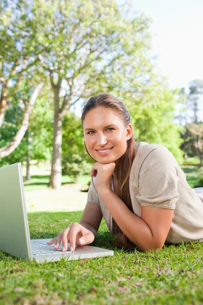 Çimenlerin üzerinde yatarken onu laptop ile gülümseyen kadın — Stok fotoğraf