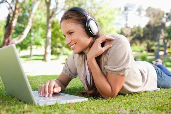 Woman with a laptop and a headset lying on the lawn — Stock Photo, Image