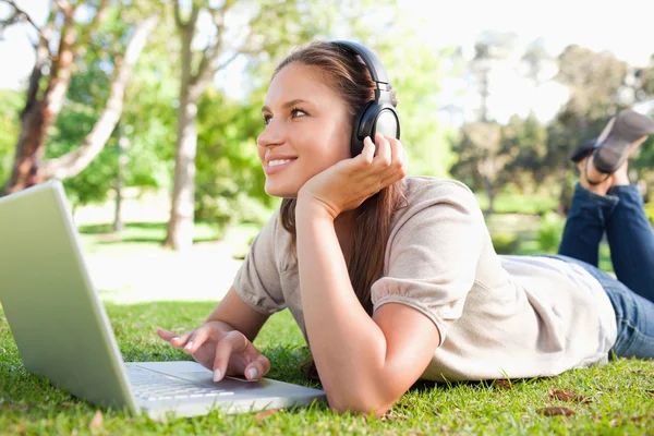 Smiling woman with headphones and a laptop lying on the lawn — Stock Photo, Image