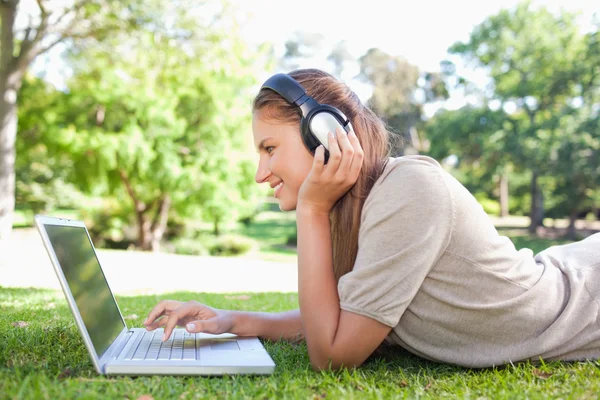 Side view of a woman with headphones and a laptop on the lawn — Stock Photo, Image