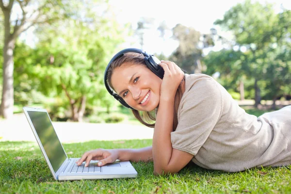 Side view of a smiling woman with headphones and a laptop lying — Stock Photo, Image