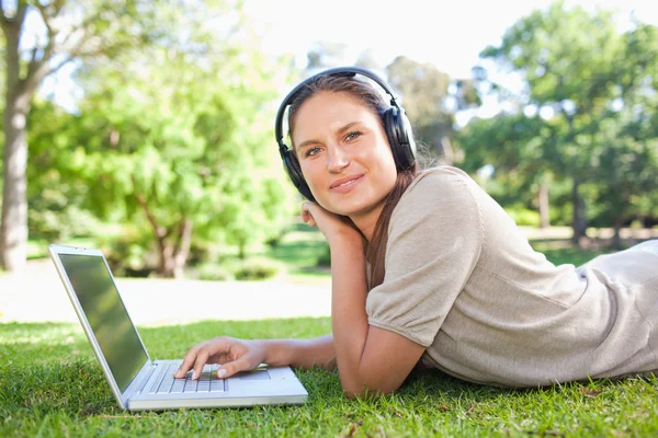 Vista lateral de uma mulher com seu laptop e fones de ouvido deitados no — Fotografia de Stock