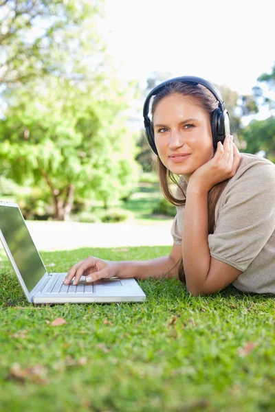 ノート パソコンとヘッドフォンと芝生の上に横たわる女性の側面図 — ストック写真