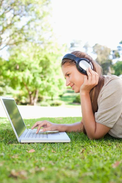Vista lateral de uma mulher com um laptop e fones de ouvido no gramado — Fotografia de Stock
