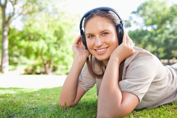 Kobieta z słuchawki leży na trawniku — Zdjęcie stockowe