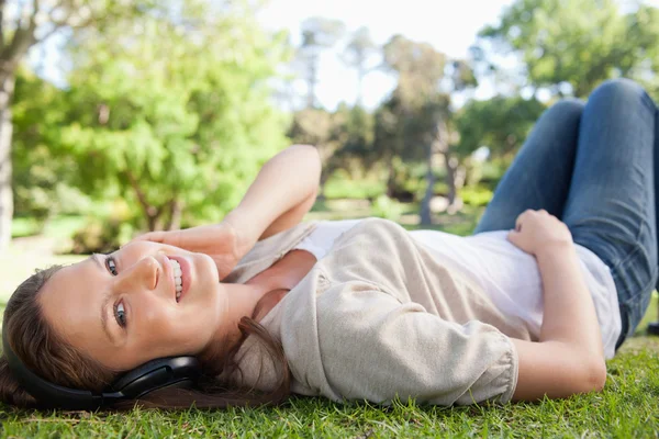 Smiling woman lying on the lawn while listening to music — Stock Photo, Image