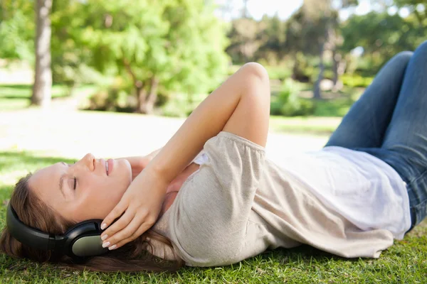 Женщина лежит на лужайке, наслаждаясь музыкой — стоковое фото