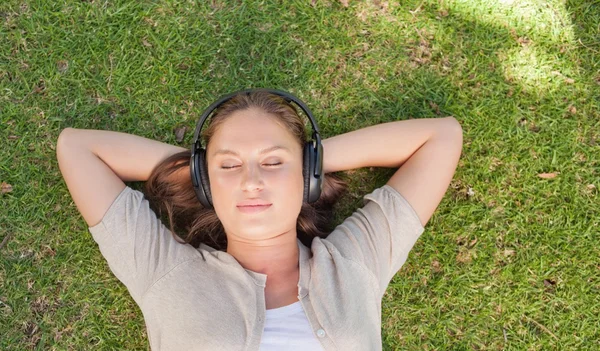 Mujer relajada escuchando música mientras está acostada en el césped —  Fotos de Stock