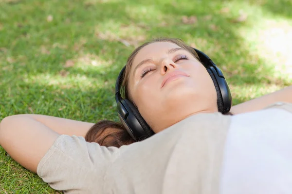 Relajada mujer acostada en el césped disfrutando de la música — Foto de Stock
