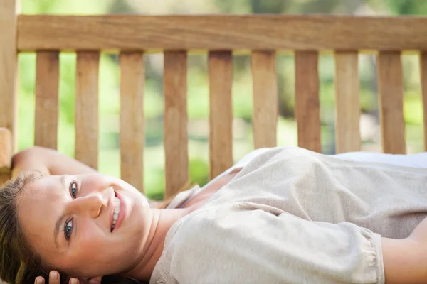 Mujer sonriente acostada en un banco del parque — Foto de Stock
