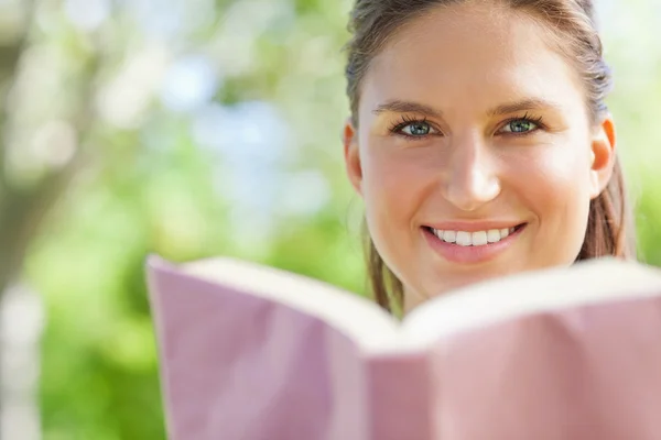 Lächelnde Frau liest im Park ein Buch — Stockfoto
