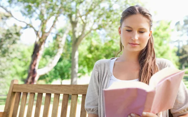 Mulher sentada em um banco de parque enquanto lê um livro — Fotografia de Stock