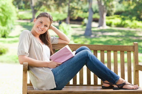 Vista lateral de una mujer sonriente sentada en un banco del parque con su bo — Foto de Stock