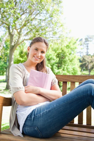 Lachende vrouw zitten op een bankje met haar boek — Stockfoto