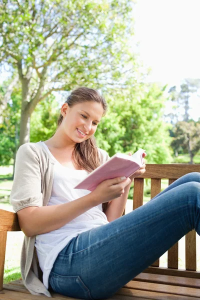 Mulher lendo um livro enquanto sentado em um banco — Fotografia de Stock