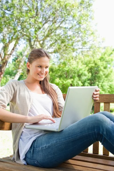 Donna sorridente con il suo computer portatile seduto su una panchina — Foto Stock