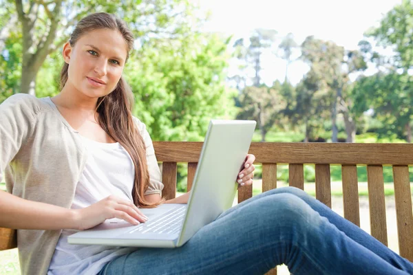 Kobieta z laptopa siedząc na ławce w parku — Zdjęcie stockowe