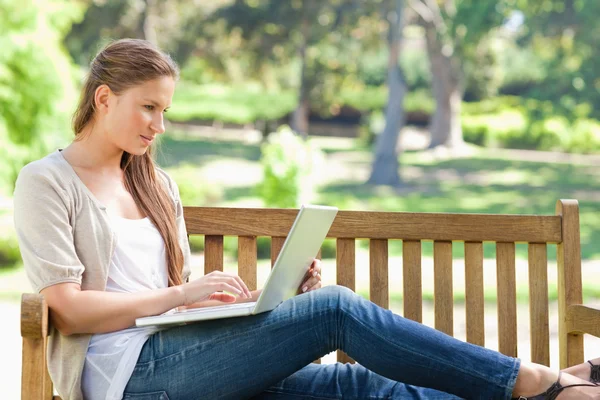 Kobieta na ławce w parku działa na jej laptopie — Zdjęcie stockowe