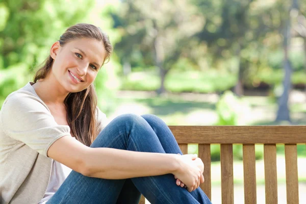 公園のベンチに座っている女性の笑みを浮かべてください。 — ストック写真