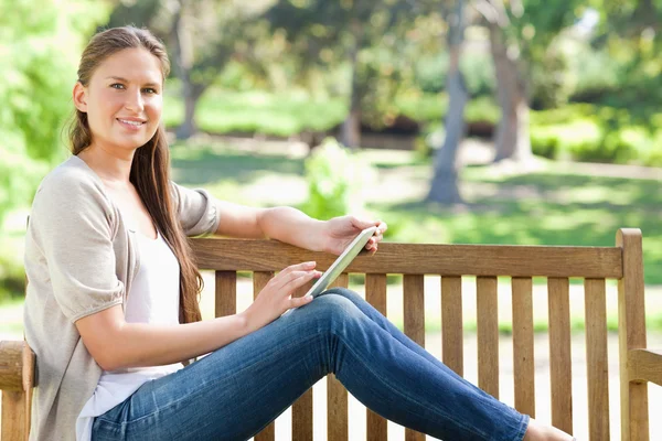 Side view of a smiling woman using a tablet computer on a park b — Stock Photo, Image