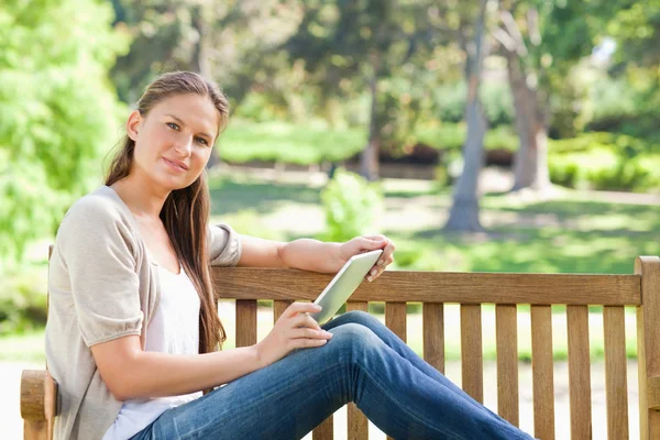 Vista lateral de uma mulher com um computador tablet em um banco de parque — Fotografia de Stock