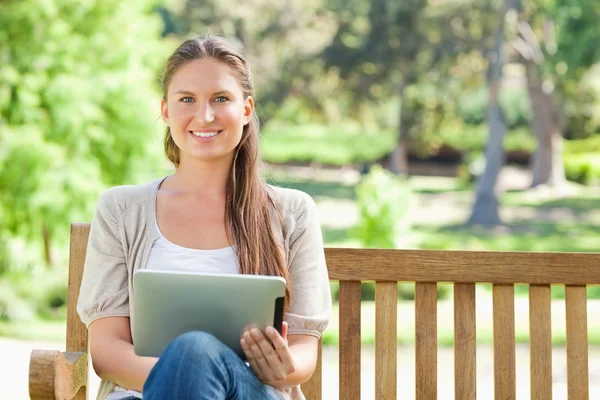 Mulher sorridente com um computador tablet em um banco de parque — Fotografia de Stock