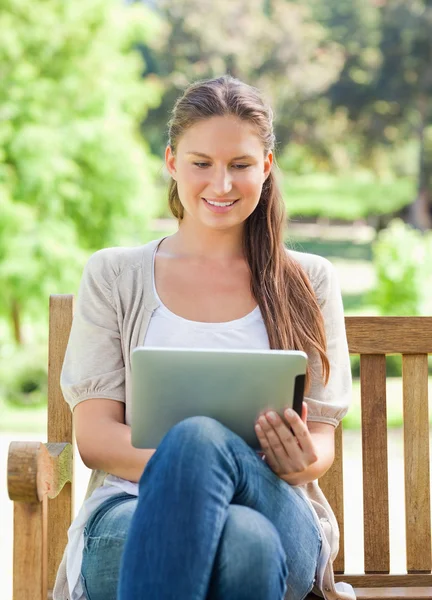 Leende kvinna använder en tablet-dator på en parkbänk — Stockfoto