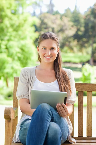 Mulher sorridente em um banco de parque com um computador tablet — Fotografia de Stock