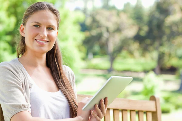 Mulher sorridente com um tablet em um banco de parque — Fotografia de Stock