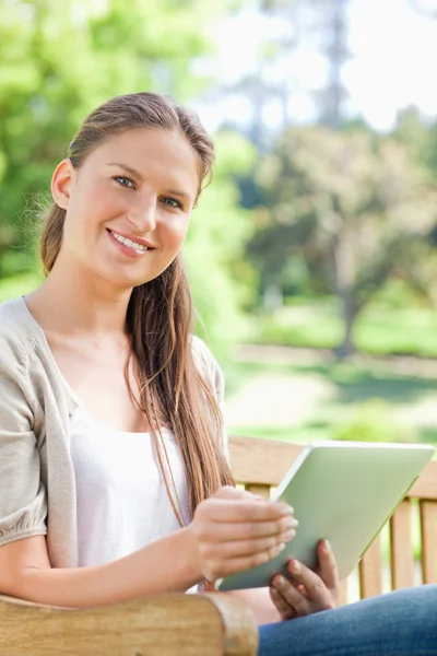 Lächelnde Frau mit ihrem Tablet auf einer Parkbank — Stockfoto