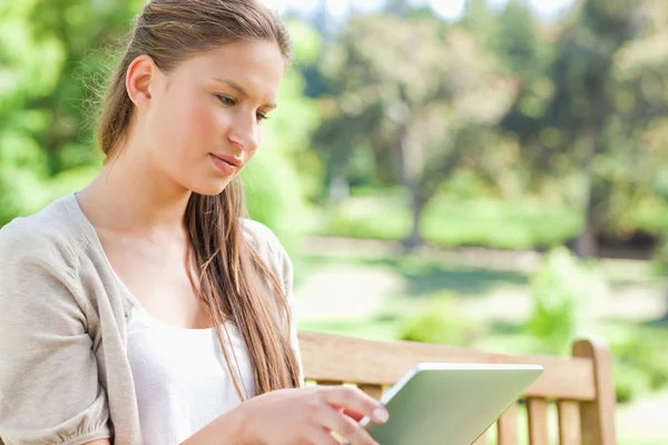 Жінка зі своїм планшетним комп'ютером сидить на лавці парку — стокове фото