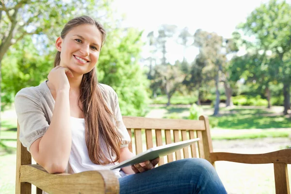 Mulher sorridente em um banco de parque com seu computador tablet — Fotografia de Stock