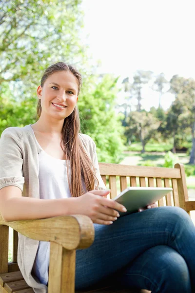 微笑着坐在长椅上与她的平板电脑的女人 — 图库照片