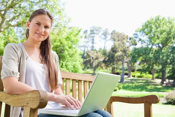 Улыбающаяся женщина с ноутбуком на скамейке в парке — стоковое фото