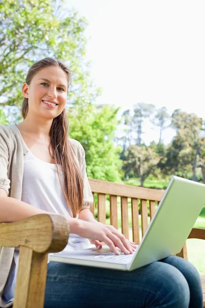 Smiling woman with her notebook sitting on a park bench — Stock Photo, Image