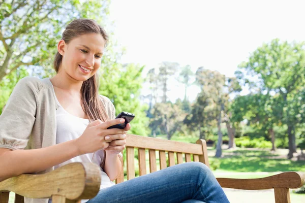 Улыбающаяся женщина читает СМС на скамейке в парке — стоковое фото